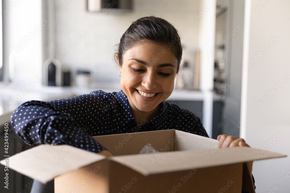 Close up smiling Indian young woman opening cardboard box with awaited online store goods at home, overjoyed satisfied customer addressee received parcel, quick postal delivery service concept Close up smiling Indian young woman opening cardboard box with awaited online store goods at home, overjoyed satisfied customer addressee received parcel, quick postal delivery service concept