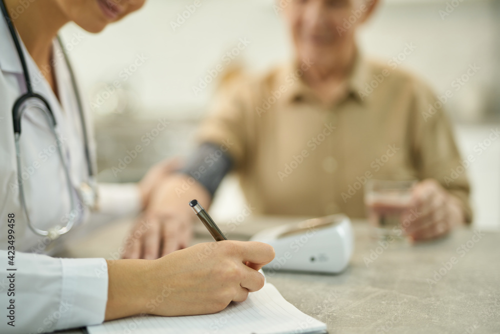 Attentive healthcare worker writing down medical conclusions about senior man