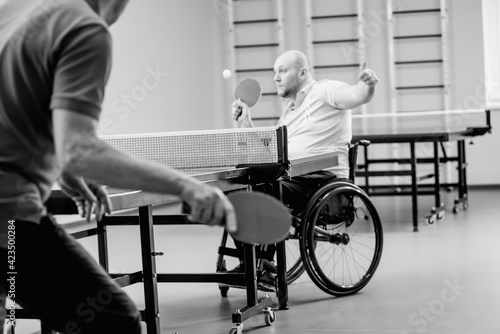 Adult disabled man in a wheelchair play at table tennis with his coach