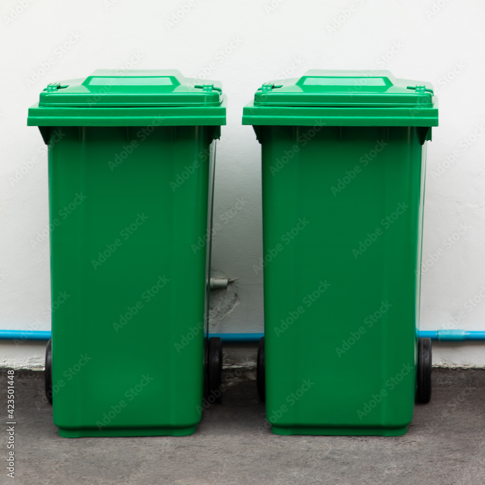 A new unbox green large bins ready to use on footpath and white concrete wall A new unbox green large bins ready to use on footpath and white concrete wall