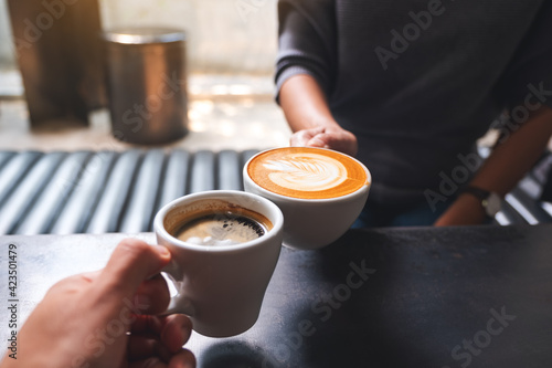 Closeup image of a man and a woman clinking white coffee mugs in cafe