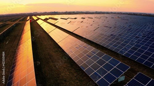 Flying above Solar Panels Stand in the fields. Sunset aerial view of Green Energy Electrical power. Ecology Innovation nature environment