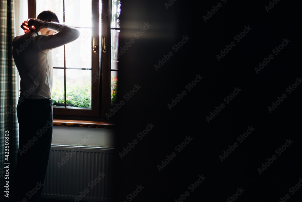 Fototapeta premium Preparing the groom for the wedding at home. The groom is preparing for the ceremony by standing at the window.