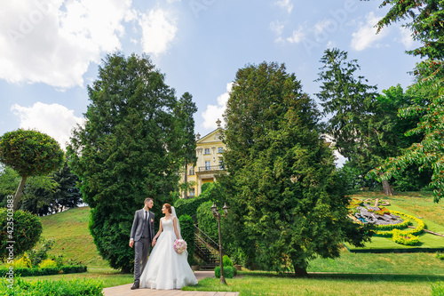 Stylish happy newlywed couple walking in the park on their wedding day.