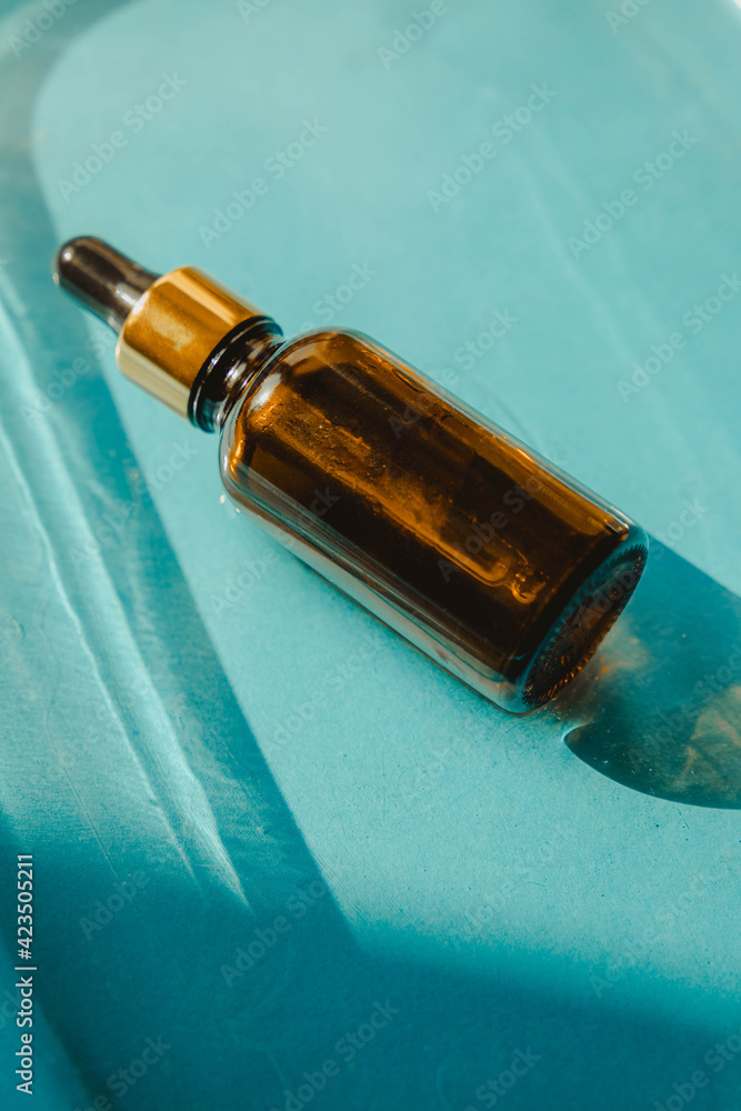 Fototapeta premium Bottle of essential oil on the water on blue background with shadow