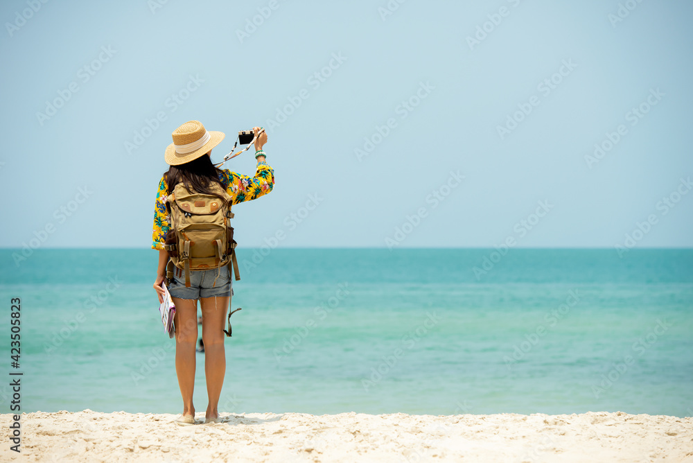 Asian woman traveler with backpack holding map take photo on the beach enjoy life Asian woman traveler with backpack holding map take photo on the beach enjoy life