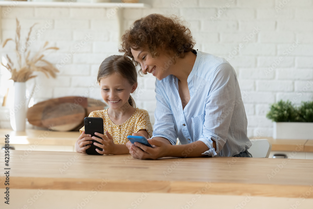 Happy young Caucasian mom and small 9s daughter relax in home kitchen ...