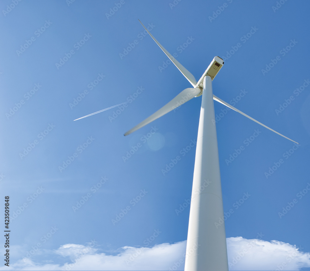 Perspectiva inferior de un molino eólico para producción de electricidad con fondo de cielo azul y estela de avión Perspectiva inferior de un molino eólico para producción de electricidad con fondo de cielo azul y estela de avión
