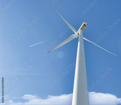 Perspectiva inferior de un molino eólico para producción de electricidad con fondo de cielo azul y estela de avión