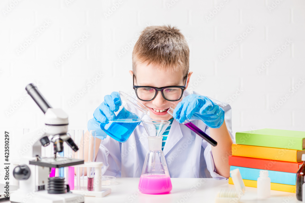A schoolboy with a microscope and book examines chemicals in test tubes, conducts experiments - a portrait on a white background. Concept for the study of coronavirus in the laboratory A schoolboy with a microscope and book examines chemicals in test tubes, conducts experiments - a portrait on a white background. Concept for the study of coronavirus in the laboratory