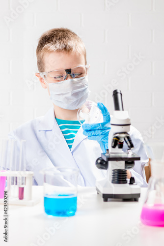 A schoolboy with a microscope examines chemicals in test tubes, conducts experiments - a portrait on a white background. Concept for the study of coronavirus in the laboratory