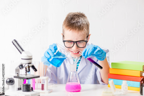 A schoolboy with a microscope and book examines chemicals in test tubes, conducts experiments - a portrait on a white background. Concept for the study of coronavirus in the laboratory