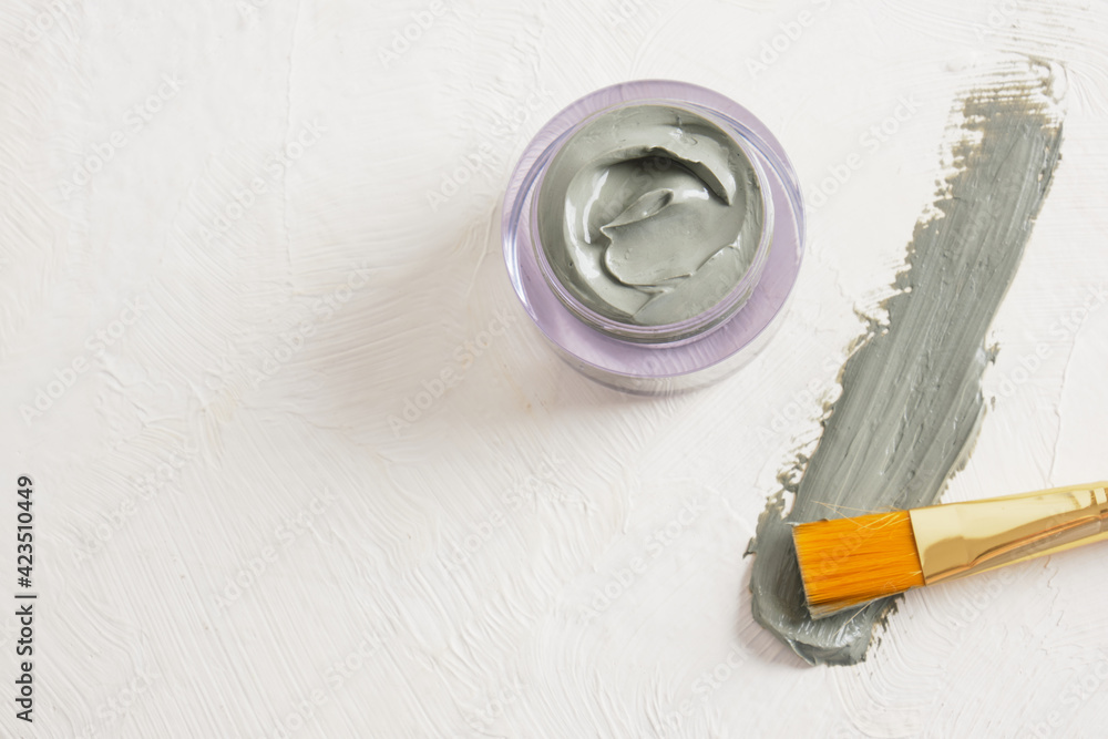 a brush for applying face masks, a jar of cosmetic blue clay and a smear of clay on a textured light background copy space a brush for applying face masks, a jar of cosmetic blue clay and a smear of clay on a textured light background copy space