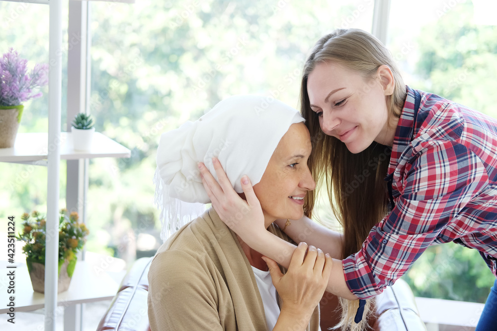 Smiling Caucasian young daughter is hugging and caring her Elderly Mother in white headscarf after chemotherapy because she is suffering from cancer or Leukemia patient. Smiling Caucasian young daughter is hugging and caring her Elderly Mother in white headscarf after chemotherapy because she is suffering from cancer or Leukemia patient.