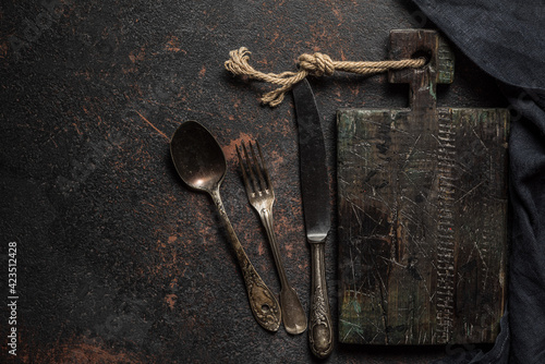 Old wooden cutting board, vintage cutlery and towel on black stone kitchen table. Top view flat lay with copy space
