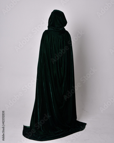 full length portrait of red haired girl wearing celtic, green medieval gown with fantasy velvet cloak. Standing pose isolated against a studio background. photo