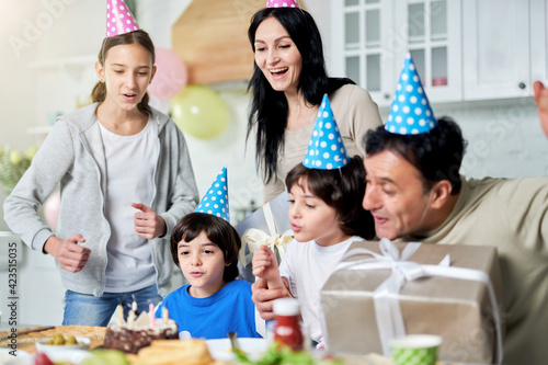 Pure joy. Joyful latin family with children wearing birthday caps, celebrating birthday together at home