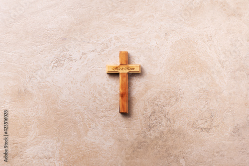 Wooden cross with text He is risen on marble background. Reminder of Jesus sacrifice and Christ resurrection. Easter passover. Palm sunday, Good friday concept. Christianity symbol and faith.