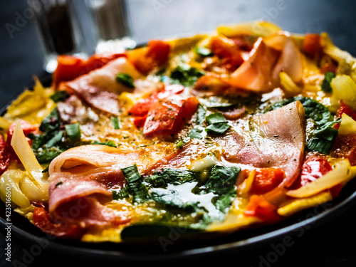 Breakfast - scrambled eggs with bacon and vegetables on black wooden table 