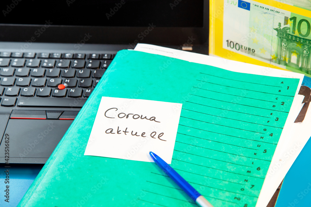 Laptop keyboard and green Folder with sticky note message aktuell, paper note and 100 Euro paper currency Laptop keyboard and green Folder with sticky note message aktuell, paper note and 100 Euro paper currency