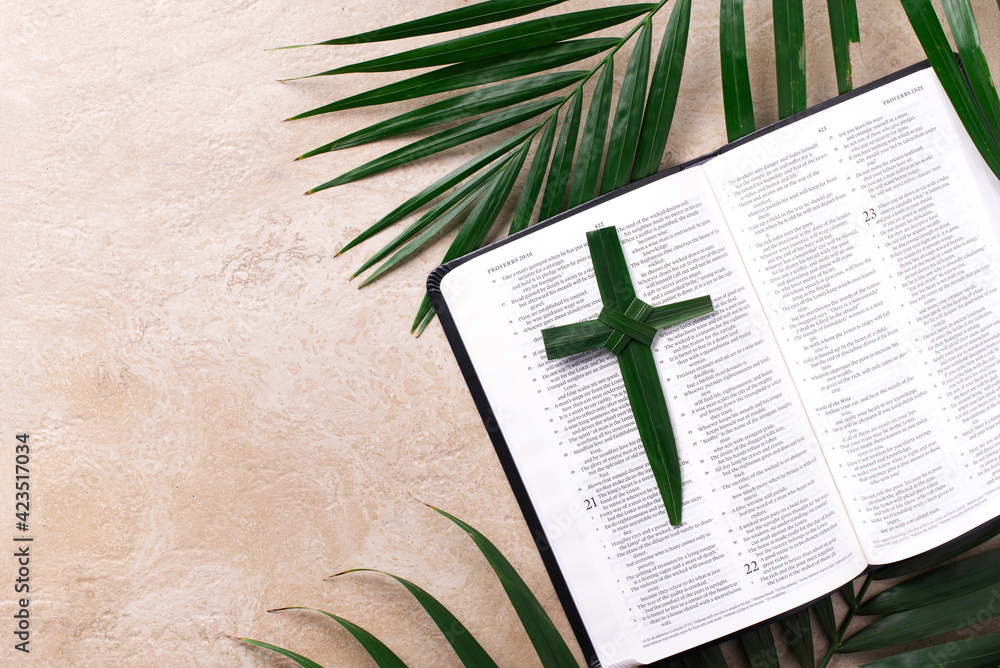Palm Sunday concept. Palm cross on open Holy Bible and palm leaves