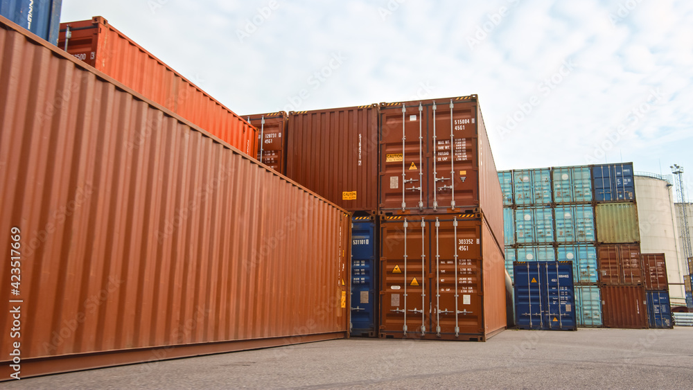 Fototapeta premium Low Angle Shot of an Industrial Terminal Location in a Shipyard Logistics Operations Center with Red and Blue Steel Shipping Cargo Containers. Daylight Cloudy Outdoors.