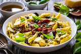 Penne with basil pesto, parmesan, black olives and sun-dried tomatoes on wooden table 
