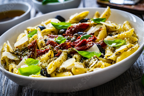 Penne with basil pesto, parmesan, black olives and sun-dried tomatoes on wooden table 