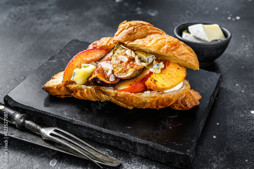 Fresh croissant sandwich with brie cheese, peach and figs. Delicious breakfast. Black background. Top view