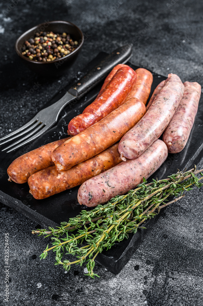Assorted raw homemade sausages on a stone board. Black background. Top view