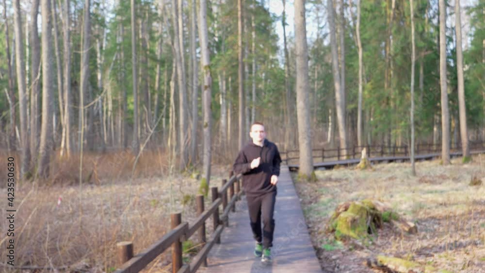 Guy in a black tracksuit runs across a brown wooden bridge. Healthy lifestyle concept Guy in a black tracksuit runs across a brown wooden bridge. Healthy lifestyle concept