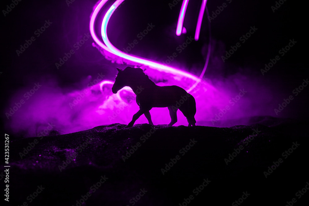 Beautiful horse running in desert at night. Silhouette of a horse miniature standing at foggy night. Creative table decoration with colorful backlight with fog. Selective focus