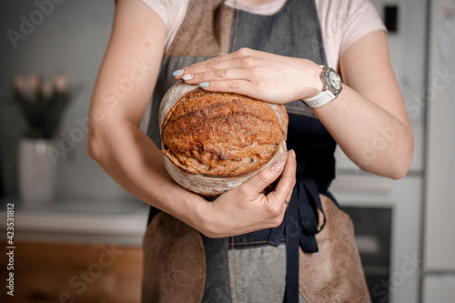 A young woman baker holds fresh baked bread in her hand. The concept of the bakery. Copy the space for the text.