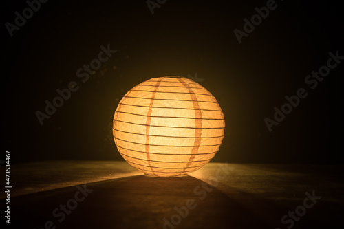 Foto Beautiful paper lantern glowing on wooden table in dark.