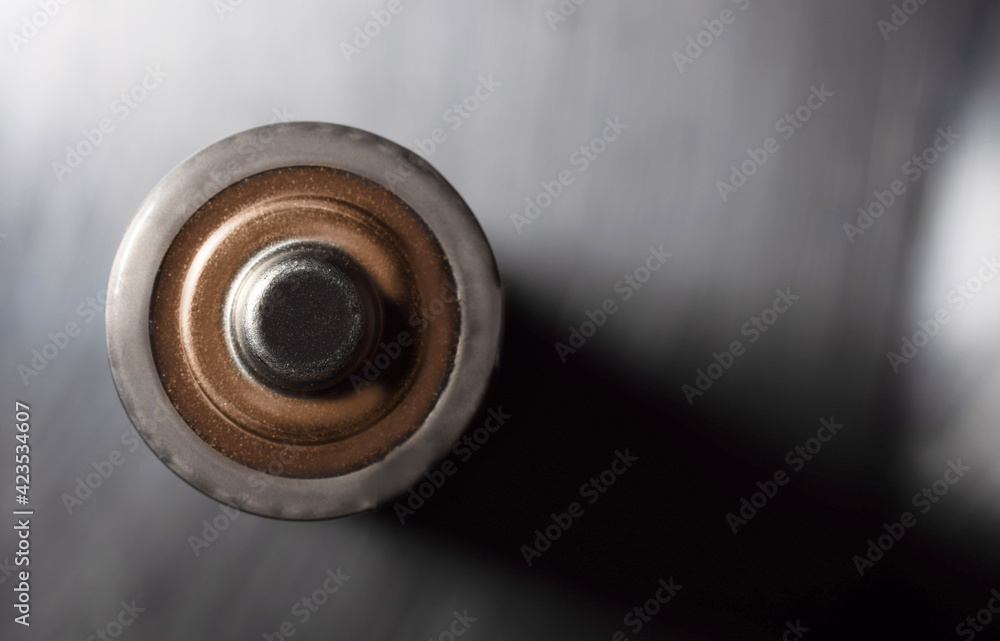 Overhead shot of a battery on a metallic gray background, with space on the right side for text. Macrophotography. Overhead shot of a battery on a metallic gray background, with space on the right side for text. Macrophotography.
