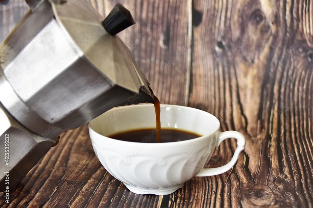 coffee pours from the coffee maker into a white porcelain cup 