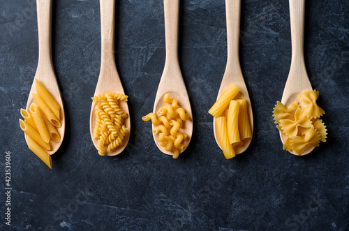 Various types of pasta on black background. Pasta in wooden spoons.