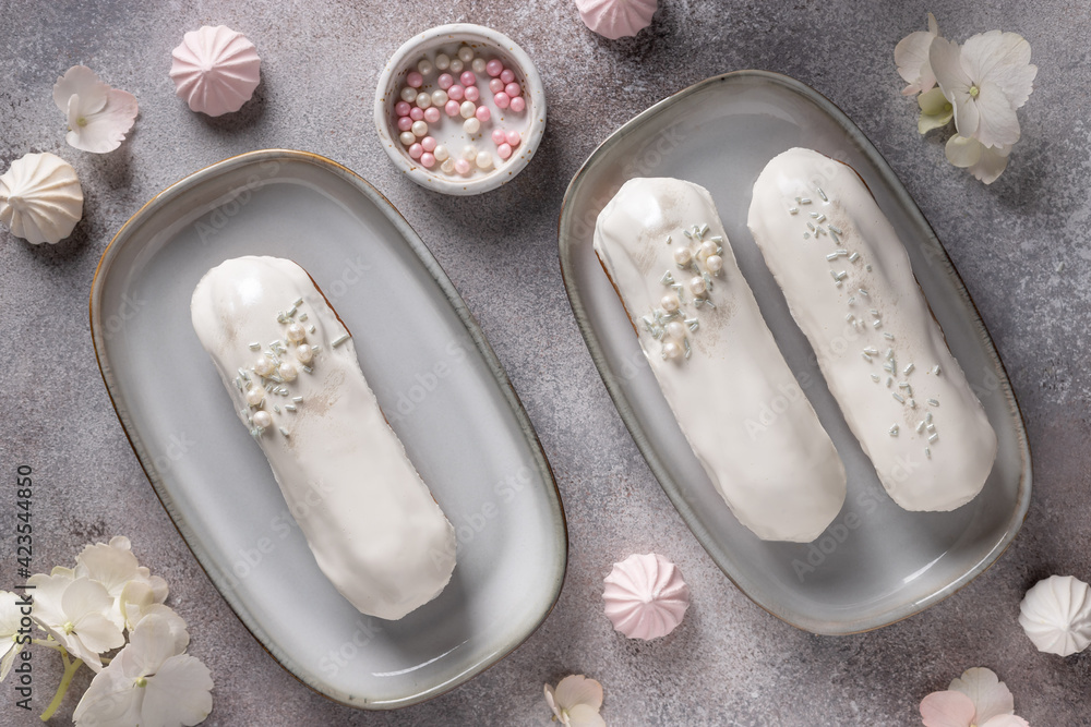 delicious eclairs with white chocolate topping on background with flowers and sweets. Pastry filled with cream. top view delicious eclairs with white chocolate topping on background with flowers and sweets. Pastry filled with cream. top view