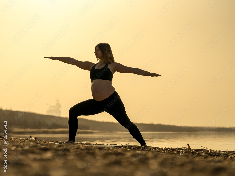 Happy pregnant woman doing yoga at a lake at a beautiful sunset