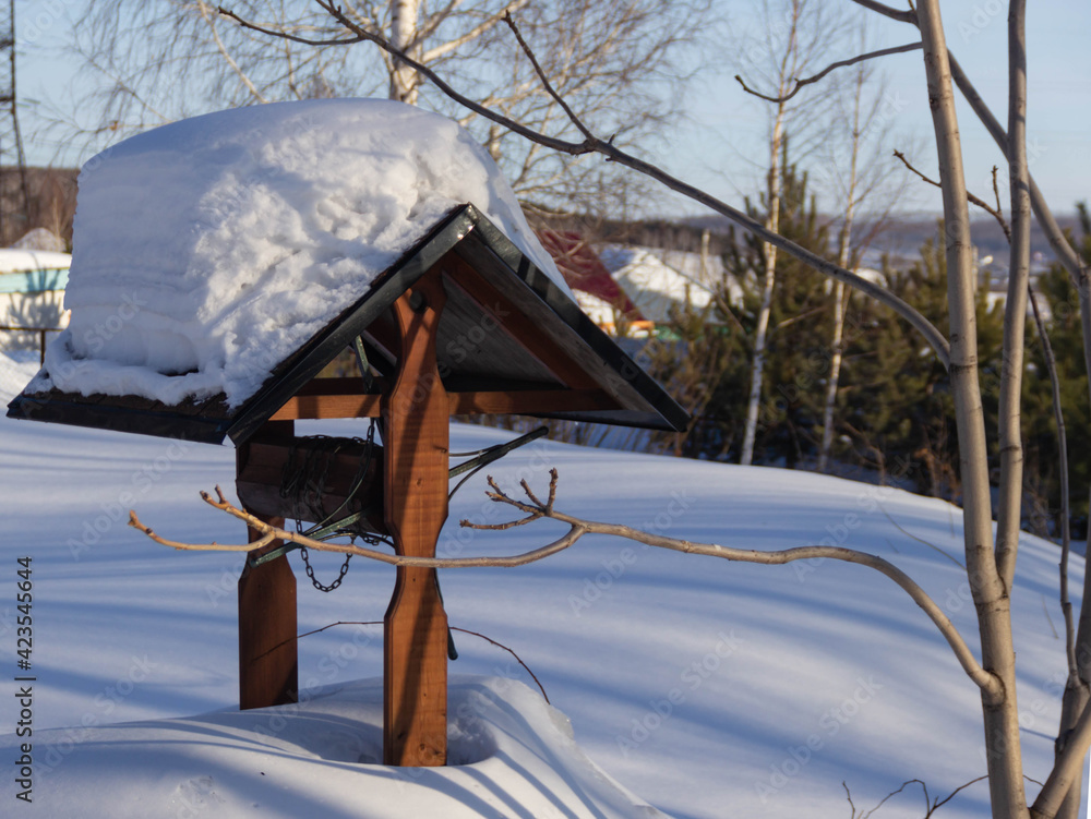the well for water extraction is covered with snow, the roof is gable the well for water extraction is covered with snow, the roof is gable