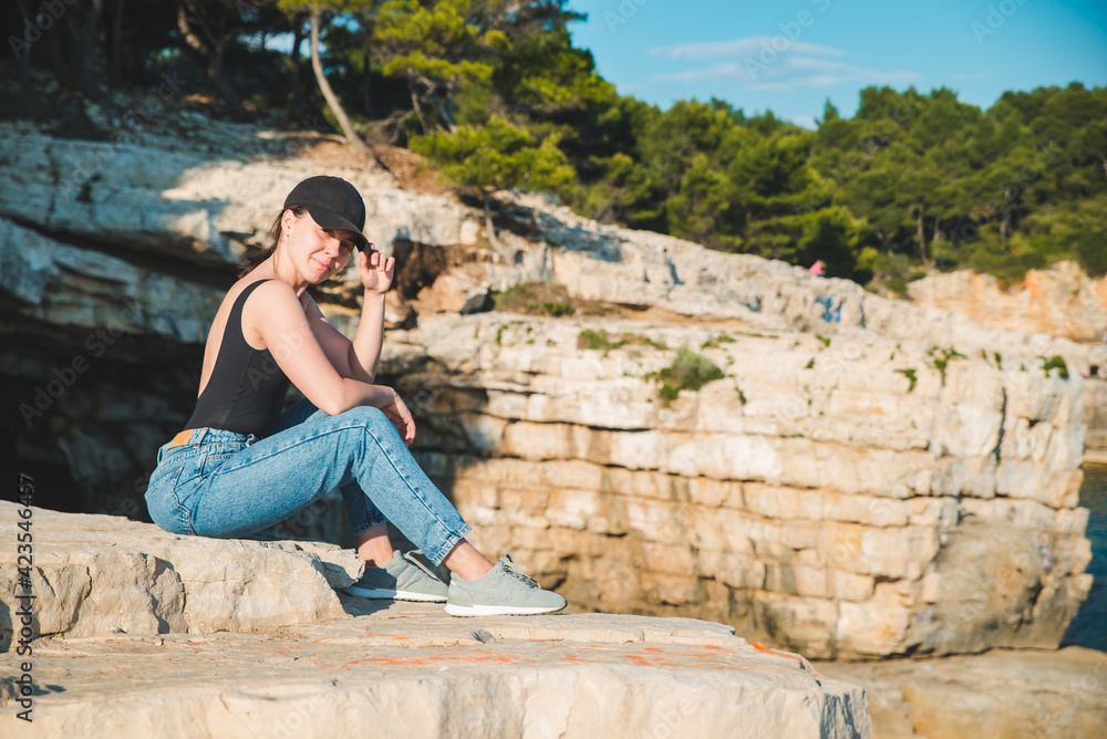 young pretty woman sitting on the cliff looking at sea young pretty woman sitting on the cliff looking at sea