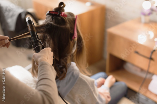 Hairdresser is preparing the girl hair style for photo shoots. Hairdresser to curl the hair in a beauty salon, barber shop. Reopening the hair salons after pandemic.