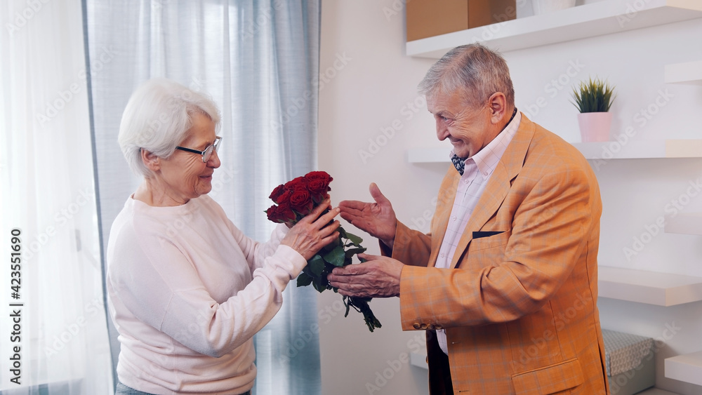 Happy elderly couple celebrating anniversary or Valentines day. Man giving bouquet of red roses to his wife. High quality photo Happy elderly couple celebrating anniversary or Valentines day. Man giving bouquet of red roses to his wife. High quality photo