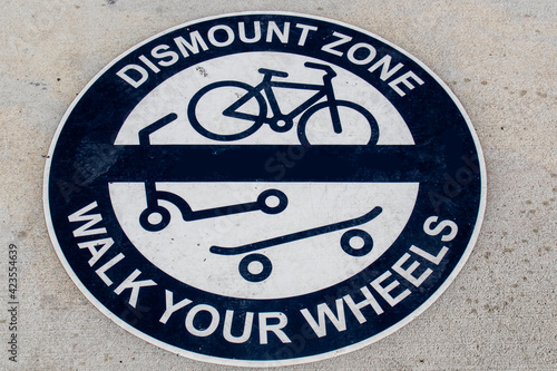 Round blue and white Dismount Zone - Walk Your Wheels sign painted on sidewalk - Grungy and view from top.