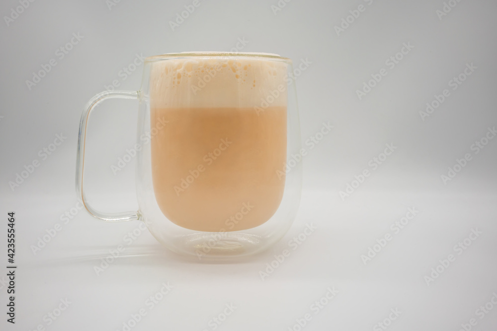 Hot Thai milk tea with milky foam sprinkle with cocoa power for decoration in double wall glass isolated on white Hot Thai milk tea with milky foam sprinkle with cocoa power for decoration in double wall glass isolated on white