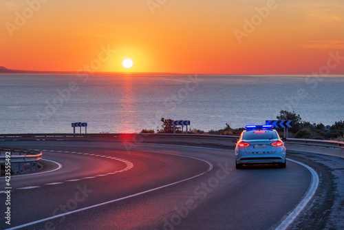 Police patrol car in charge of monitoring traffic on the roads, driving on a mountain road with the sea and the sun on the horizon.