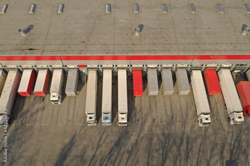 Aerial view of goods warehouse. Logistics center in industrial city zone from above. Aerial view of trucks loading at logistic center. View from drone.