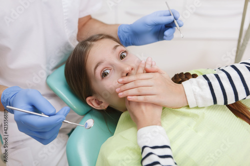 Young scared girl covering her mouth refusing dental examination by dentist