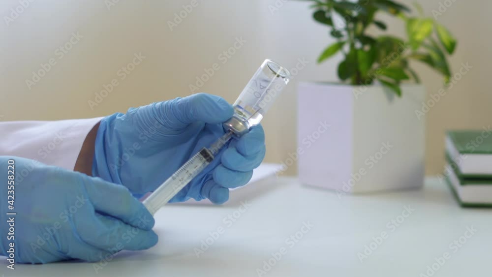Doctor drawing up vaccine from phial bottle and filling syringe