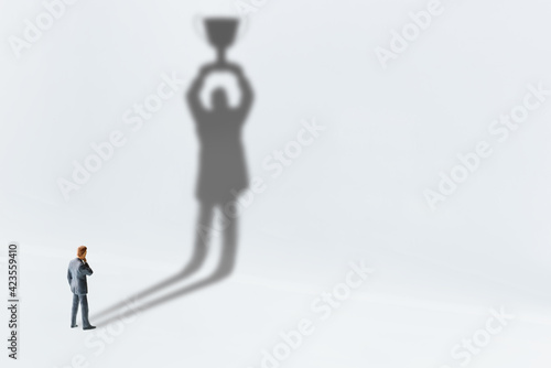 Comtemplating on business success, top performance, winner concept : Businessman looks his shadow raising a trophy cup on the wall, depicts scrutinizing on ways to race and achieve goals and win prize
